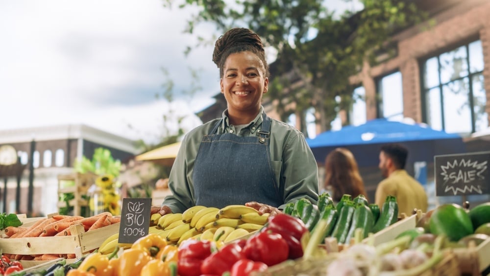 woman standing behind farm stand with fruits and vegetables