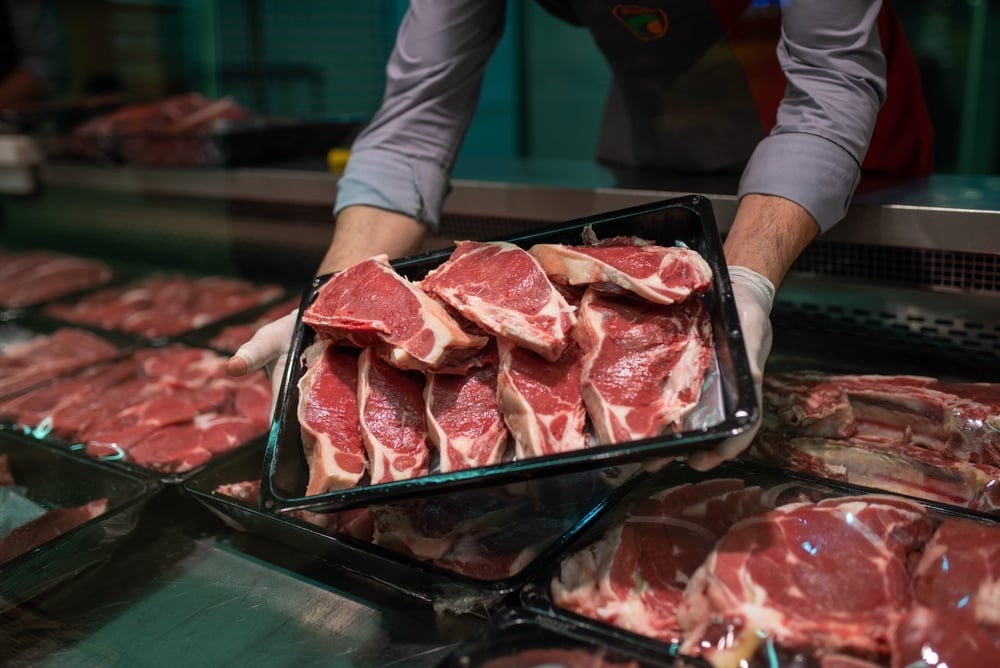 employee reaching into meat cooler pulling out steaks