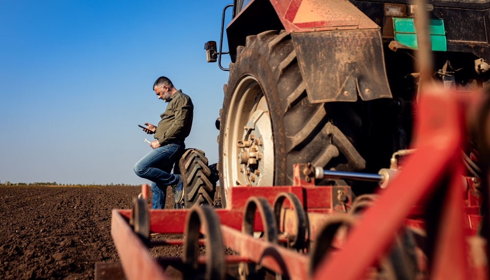 farmer leaning against tractor looking at iphone